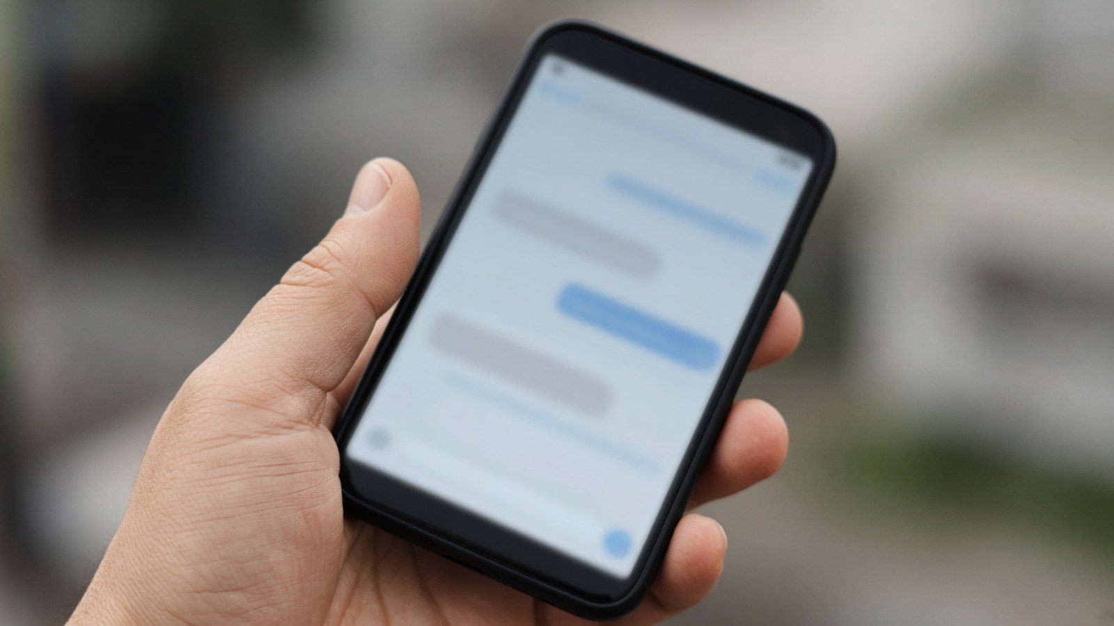 Detail ruky držiacej smartfón s otvorenou textovou správou, na displeji je rozmazaný odkaz